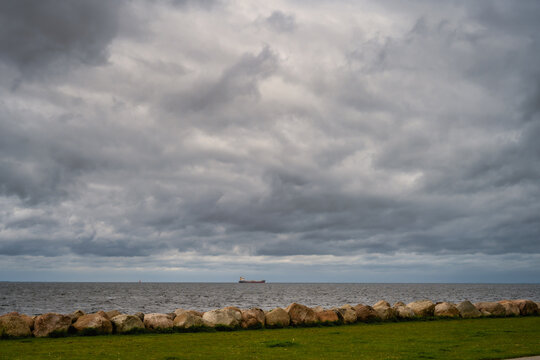 A beautiful, dramatic sky over the ocean. A lawn and stones in a wave breaker in the foreground. Picture from Malmo, Sweden