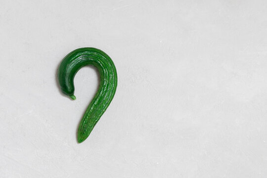 Funny ugly cucumber shapes as question mark on neutral background. Image with copy space, top view