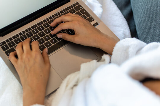 Close up of a female on a couch working on a computer and wearing a bathrobe