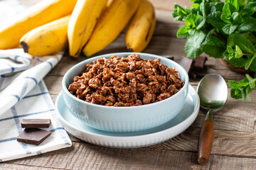 Chocolate oatmeal for breakfast with slices of a ripe banana and pieces of bitter good chocolate in a ceramic bowl on a wooden background. Example of a healthy breakfast