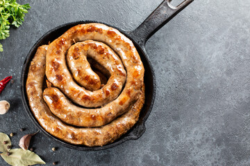Grilled spiral sausage with spices in a frying pan on a stone background. Top view from above and...