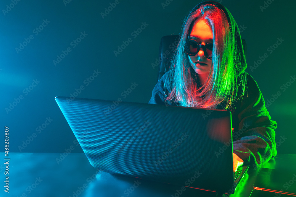 Poster woman hacker next to a laptop. girl hacker in the neon light. hacking. woman cracker works in the da