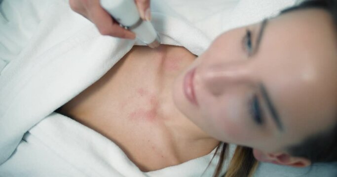 Close-up a female client in a bathrobe is laying in the cosmetology bed while having a non-injection bio revitalization procedure by using the Dermadrop TDA device.