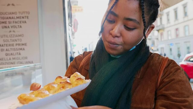 Smiling young woman eating pastry outdoors, Italy