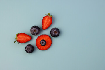 Halves of strawberries and blueberries on a blue background. Fresh strawberries and blueberries. Juicy summer background. 
