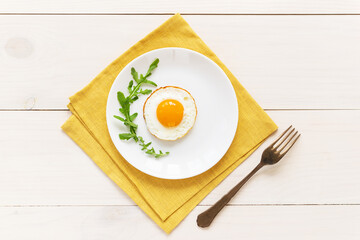 Fried eggs with arugula in a plate on a yellow linen napkin. Horizontal orientation, top view.
