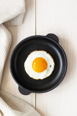Fried eggs in a skillet on a wooden table. Vertical orientation, top view.