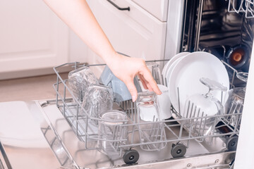 Built-in dishwasher, dishwashing. A woman loads washed dishes, cups, glasses. A woman's gentle hand puts something in the dishwasher or pulls out, unloads.