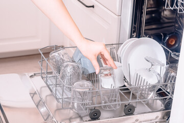 Built-in dishwasher, dishwashing. A woman loads washed dishes, cups, glasses. A woman's gentle hand...