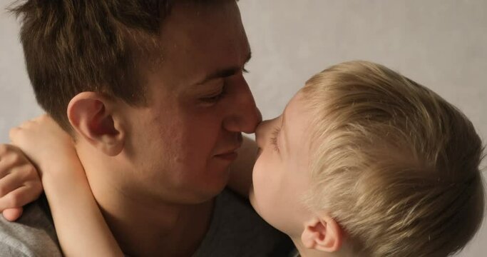 Dad and son rub their noses on each other, the boy tells something. Kid hugs daddy. Tenderness between parent and child