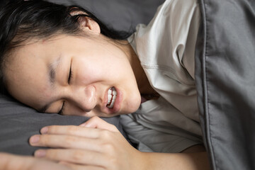 Asian lady girl suffering from bruxism while lying in bed at night,female grinding of the teeth during sleep,teeth clenching,sleep disorders,oral health problems,dental care,sleep bruxism concept