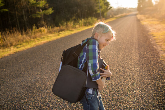 Smiling boy with books on rural road at sunset