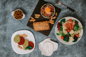 Fototapeta na wymiar Meat platter and Camembert cheese with baguette. Salad with prosciutto. Olives. Perfect fried eggs with mushrooms and spices. Vegan vegetable cutlets and peanuts. Fork. Food delivery.
