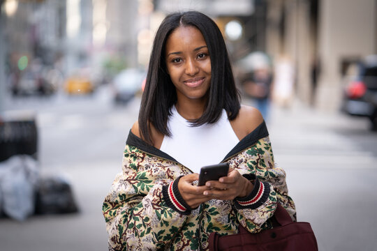 Young black woman in city walking street using cellphone