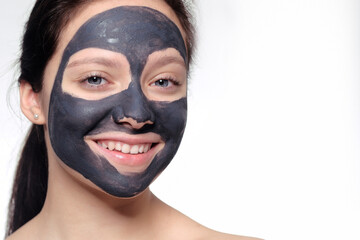 Teenager girl in a black mask, natural photo of a real mask on a young girl. Texture dark cream. Model on a white background smokes skin