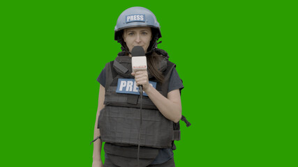 GREEN SCREEN CHROMA KEY Caucasian female war journalist wearing protective helmet and bulletproof vest reporting live in front of the camera - obrazy, fototapety, plakaty