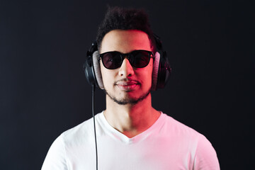 Smile Young African American man portrait wearing headphones and enjoy music over black Background. Red light reflection on face.