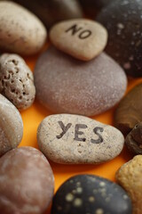 Fototapeta na wymiar Pebble stones with the text yes and no on an orange table. Other clean pebbles around