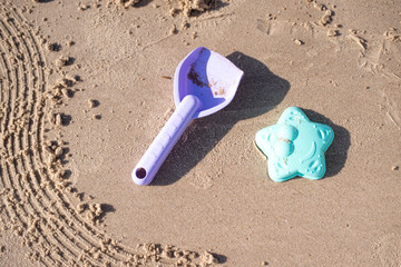 Fototapeta na wymiar Children's beautiful delicate coloring toys: shovel and mold placed on sand. Sandy seashore. Kid play on beach. Family’s vacation on sea. Summer time.