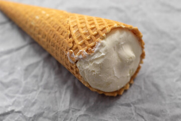 On the white crumpled paper is a close-up of an ice cream in a whole waffle cone