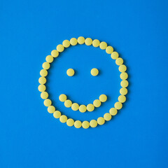 Smiling face from yellow round pills on blue background. Tablets, vitamins, medicine concept.