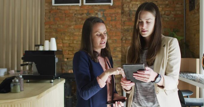 Caucasian female business owner and her coworker using tablet and talking