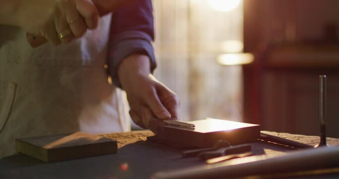 Close up of hands of caucasian female jeweller using hammer, making jewelry