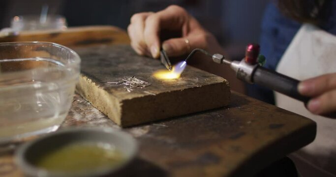 Close up of hands of caucasian female jeweller using gas burner, making jewelry