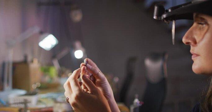 Close up of hands of caucasian female jeweller wearing glasses, checking jewelry at workshop