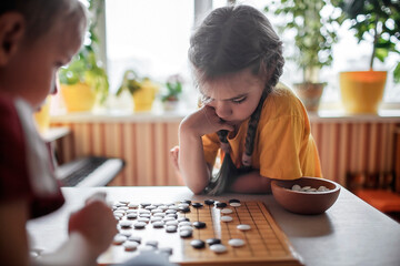 Brother and sister playing Chinese chess go at home, sibling have fun together with igo go stones,...