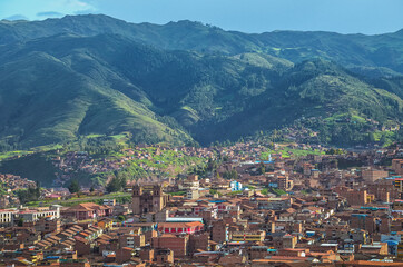 Aerial view of rooftops in Cusco city with the valley surrounded by green in the bottom. Houses and...