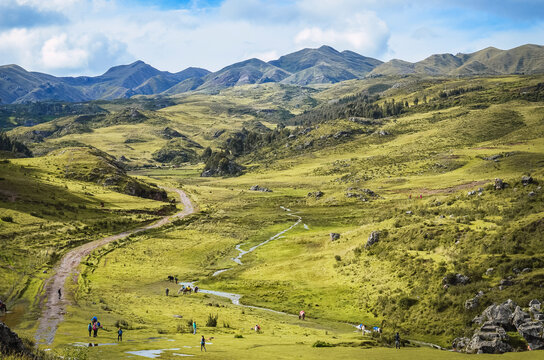 Outstanding view of a road with people and horses in middle of green fields near Qenqo Archaeological Site. Beautiful landscape hills of Cusco, Peru, South America