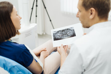 Male Professional Dentist With Gloves And Mask Holding papers photo And Show What The Treatment Will Look Like Of The Patient's Teeth. Discussion Of The Treatment Plan And Healthy Smile