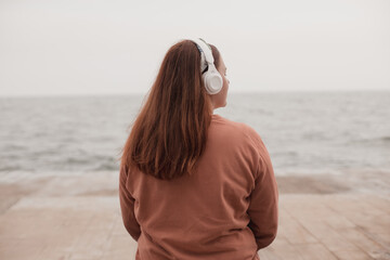 Obraz premium Relaxed cute girl listening to music on the beach at sea background. Back view