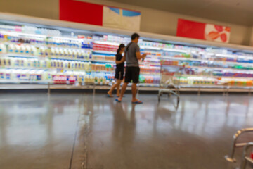Defocused blur of male and female cart  buying milk in supermarket