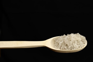 Sea salt crystals in wooden spoon on black background