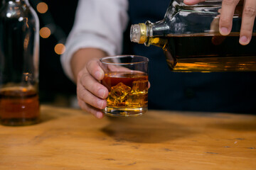 Waitress man standing pours whiskey into a glass celebrate whiskey on a friendly party in restaurant