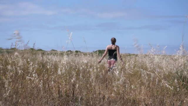 Woman Walking Away Through Field, Slow Motion. Young woman is walking away through a beautiful field on a bright sunny day. Slow motion