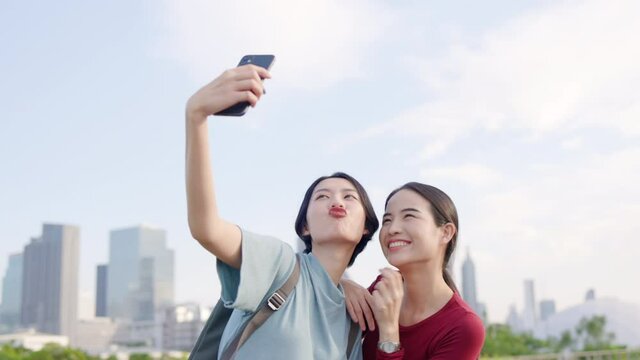 Two Beautiful Asian teenage woman using smartphone to take selfies. Tourists happy take pictures from mobile phones while traveling in city. Freedom to travel with safety. Concept travel insurance