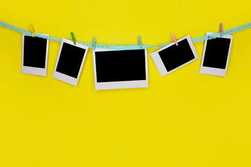White photo cards hang on string with clothespins in row of frames. Yellow background.