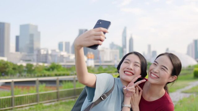 Two Beautiful Asian teenage woman using smartphone to take selfies. Tourists happy take pictures from mobile phones while traveling in city. Freedom to travel with safety. Concept travel insurance