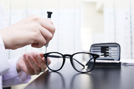 Eyeglass repair. Close-up of the hand of a master who uses a screwdriver to tighten a screw in a spectacle frame. Optics salon and repair shop