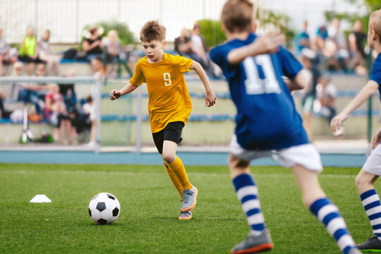 Young Boy Running Fast and Kicking Soccer Ball on Grass Pitch. Football Tournament For Youth School Teams. Group of Children in Jersey Unifrom Playing Sports. Football Fans and Parents in Background