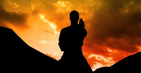 Composition of silhouette of male martial artist over orange sky with sun setting