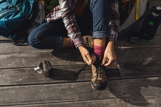 Low section of caucasian woman camping, sitting outside tent on deck putting on boots
