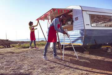 Diverse couple opening and preparing food truck by seaside on sunny day