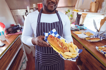 Midsection of african american man in food truck holding hotdog and chips