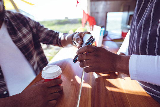 Midsection of african american man in food truck taking smartphone payment holding terminal