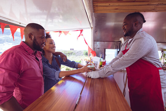 Smiling african american man in food truck chatting to male and female customers