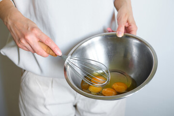 A woman beats eggs in a bowl with a whisk. Cooking an omelet. The chef prepares breakfast in the kitchen. A healthy tasty egg recipe. Cooking home cooking for the family